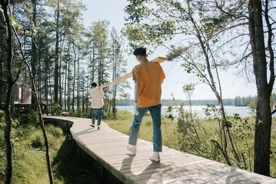Two men carrying wooden planks on a forest boardwalk by a lake.