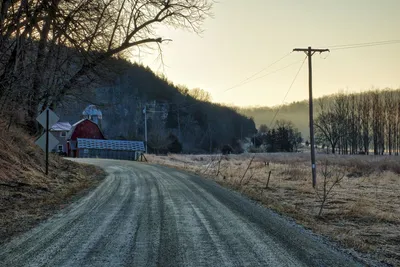 Peaceful rural road in Minnesota during fall, featuring a classic red barn and barren trees.