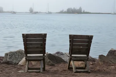 Two wooden chairs on a sandy beach in Grand Marais, MN, offering a peaceful view over a calm lake.