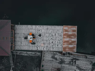 Drone shot of a wooden dock beside a lake, featuring people sitting around a table with visible shed structures.